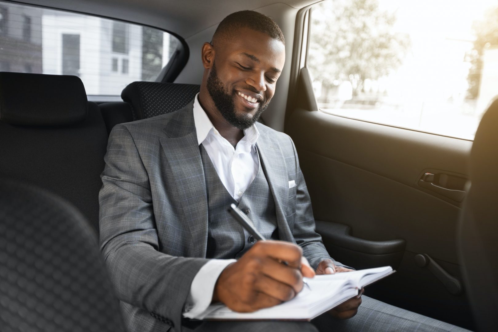 happy-black-businessman-sitting-in-car-taking-notes